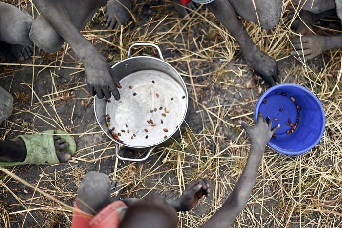 Niños recogen el grano derramado de bolsas de yute que se rompieron luego de una entrega de alimentos desde un avión, en una aldea en el condado de Ayod, Sudán del Sur (archivo, febrero de 2020). · Foto: Tony Karumba, AFP