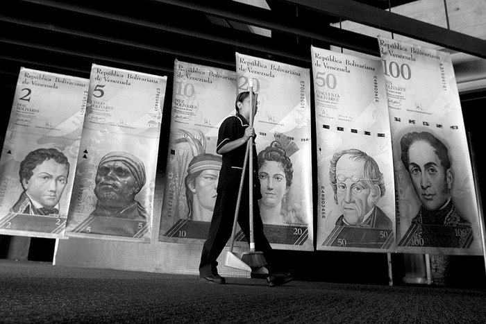 Una limpiadora pasa frente a afiches de billetes venezolanos, ayer, en la sede del Banco Central de Venezuela, en Caracas (Venezuela). Foto: Miguel Gutiérrez, Efe