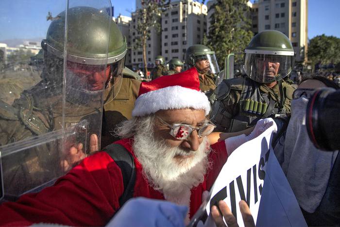 Un manifestante disfrazado de Papá Noel es detenido por la policía antidisturbios, durante una protesta contra el gobierno del presidente chileno Sebastián Piñera, en Santiago. · Foto: Claudio Reyes, AFP