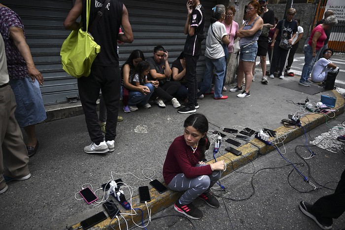 Personas cargan sus teléfonos móviles desde un camión del municipio de Chacao durante un apagón en Caracas. · Foto: Juan Barreto, AFP