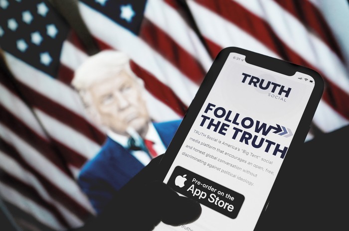 Revisando la tienda de aplicaciones en busca de "Truth Social" frente a una foto del expresidente estadounidense Donald Trump en Los Ángeles, California. · Foto: Chris Delmas, AFP