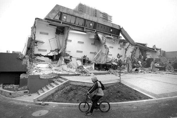 Un hombre pasa en bicicleta junto a un edificio destruido, ayer, en Concepción (Chile).  · Foto: EFE, Ian Salas