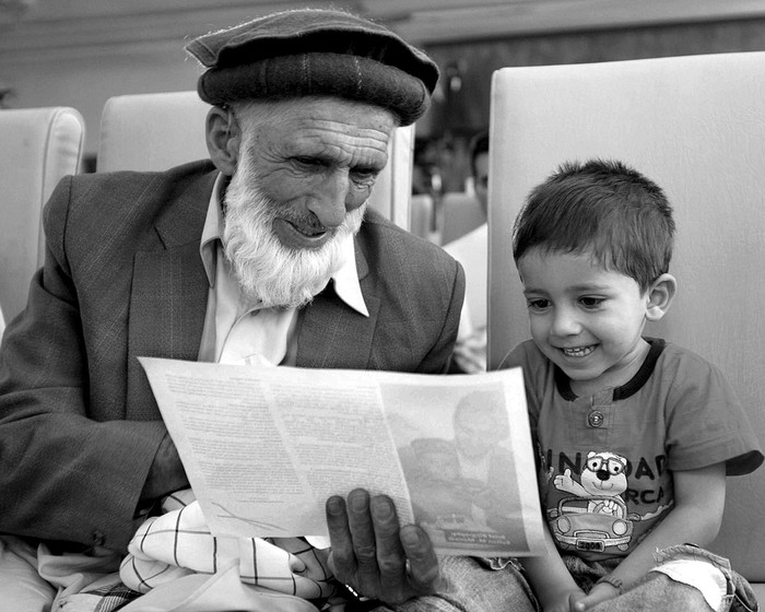 El padre del periodista afgano Sultan Munadi muestra fotografías de su hijo a su nieto, el domingo en Kabul, Afganistán. · Foto: EFE, s/d de autor