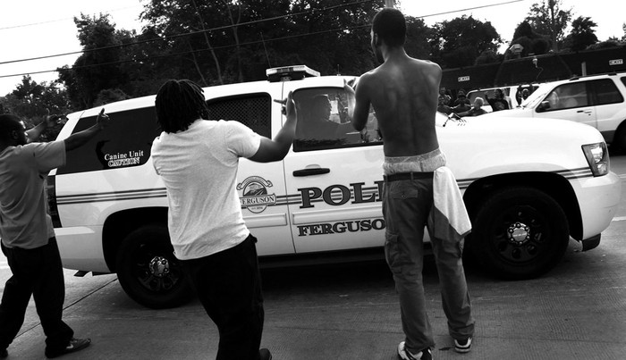 Manifestantes gesticulan mientras pasa un coche de la Policía de Ferguson, en la calle West Florissant Road ayer, cerca de St. Louis, Missouri (Estados Unidos). / Foto: Robert Cohen, Efe.