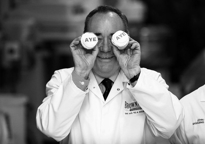 Alex Salmond, líder independentista y ministro principal escocés, con dos pasteles en los que se lee "Aye" ("Sí", en inglés y escocés), durante su visita a una fábrica pastelera en Kilmarnock, Escocia (Reino Unido), el 3 de setiembre de 2014. / Foto: Robert Perry, Efe