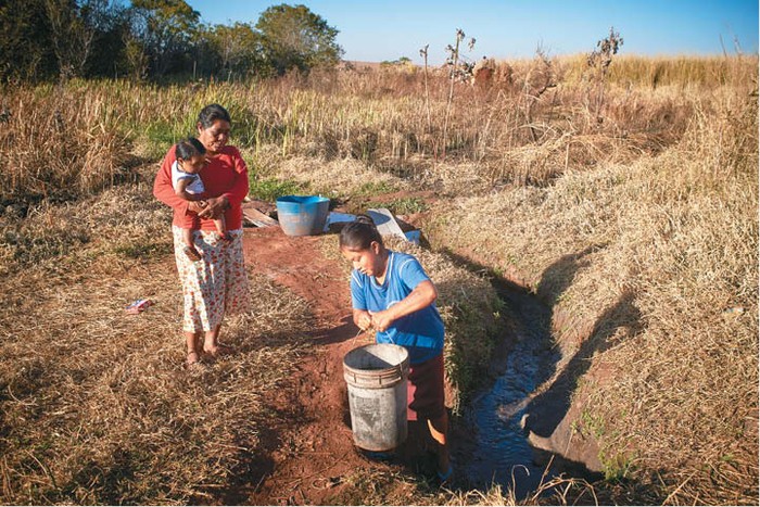 Doña Leandra y su hija recogen agua en la única naciente disponible en su territorio. A pesar de que el agua se encuentra contaminada por agrotóxicos, la utilizan para beber, cocinar y bañarse. Retomada de Tey’i Jesu, Caarapó.