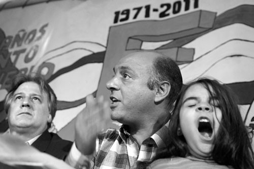 Fernando Lorenzo, ministro de Economía y Finanzas, junto a Marcelo Abdala, coordinador del PIT-CNT, y su hija, durante la charla debate “¿Hacia dónde va la economía nacional? El gobierno y los trabajadores debatimos juntos”, en el comité Cuaró del Frente Amplio, en el barrio La Teja de Montevideo. · Foto: Nicolás Celaya