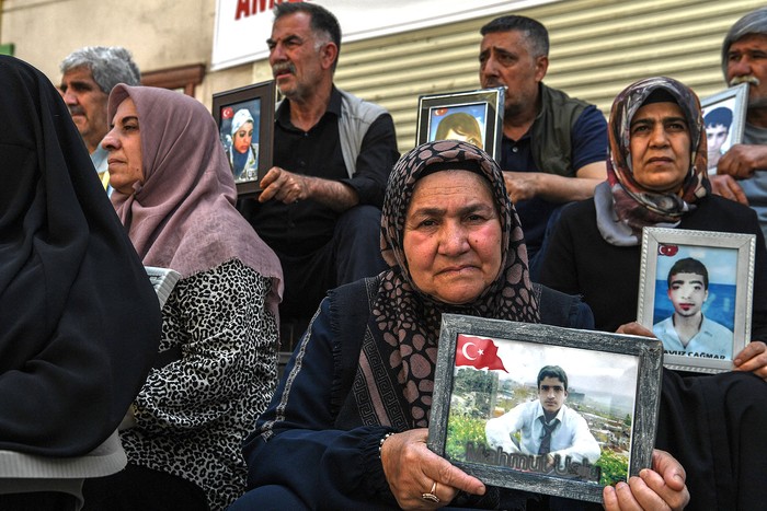 Familias cuyos hijos se unieron al PKK sostienen sus imágenes sentadas frente a la sede del Partido Igualdad y Democracia tras el anuncio del PKK de su disolución, el 12 de mayo, en la ciudad de Diyarbakir, de mayoría kurda, al oeste de Turquía. · Foto: Ilyas Akengin, AFP