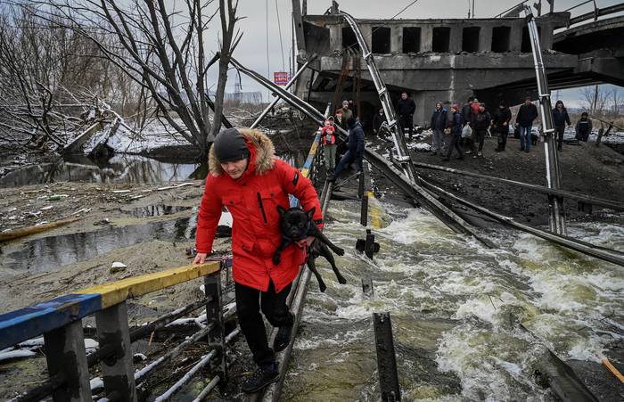 Civiles ucranianos cruzan un río con el puente destruído, este martes, en el frente norte de Kiev. · Foto: Aris Messinis, AFP