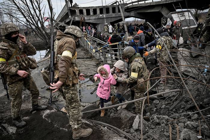 Civiles cruzan un puente destruido ayudados por militares ucranianos, mientras evacuan la ciudad de Irpín, al noroeste de Kiev, el 5 de marzo de 2022. · Foto: Aris Messinis, AFP