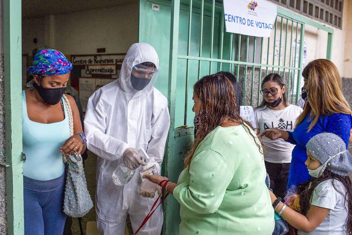 Un funcionario electoral rocía desinfectante en las manos de un votante a la entrada de un colegio electoral, el 21 de noviembre, en Caracas. · Foto: Cristian Hernández, AFP